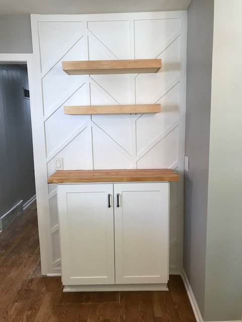 Accent wall with geometric trim, floating wood shelves and a cabinet