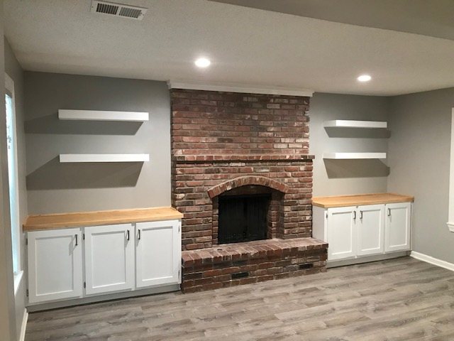 Built-in cabinets with butcher-block tops and floating shelves beside a brick fireplace