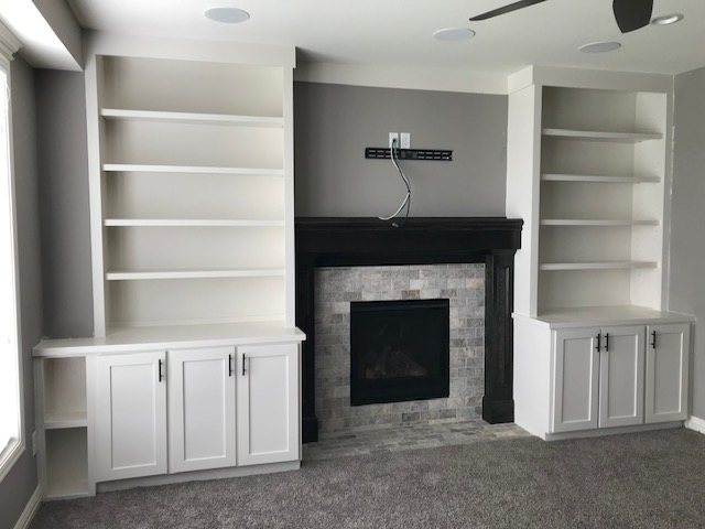 White built-in bookshelves and cabinets flanking a tiled fireplace with a dark mantel