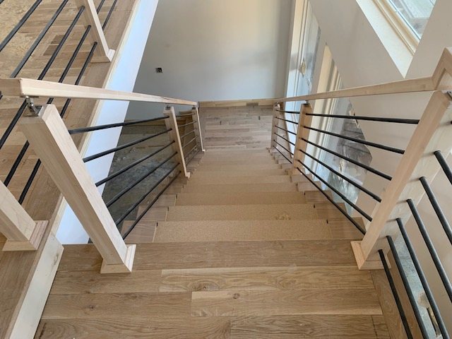 Wide oak staircase with horizontal black metal railing and square oak posts